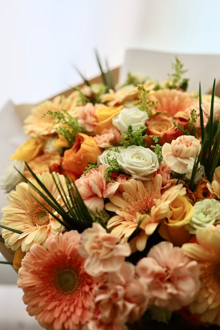A vibrant floral arrangement featuring a mix of peach, cream, and soft pink roses, complemented by peach gerbera daisies and delicate pink lisianthus, all accented with green foliage including palm le